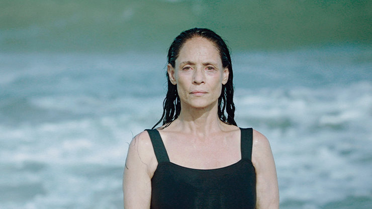 Mulher branca de meia idade com o cabelo preto molhado, penteado para trás.